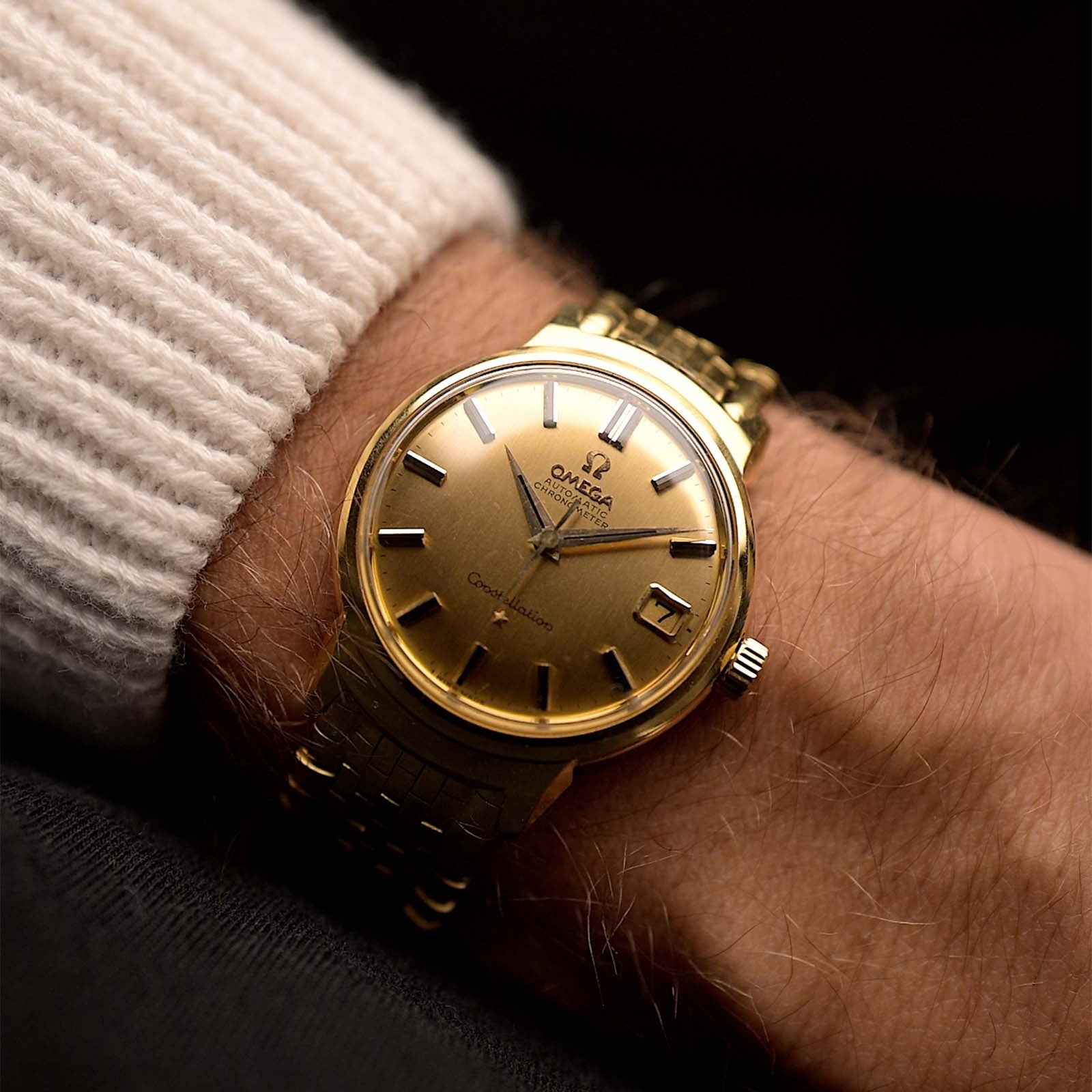 ساعة أوميغا كونستيلايشن 14398 دي لوكس ذهبية عتيقة من أوميغا كونستيلايشن 14398 دي لوكس من عام 1960 على معصم على خلفية سوداء. عرضها 34 مم، ذهب أصفر عيار 18 قيراط، حركة أوتوماتيكية عيار 561، مينا ذهبي وسوار ذهبي.