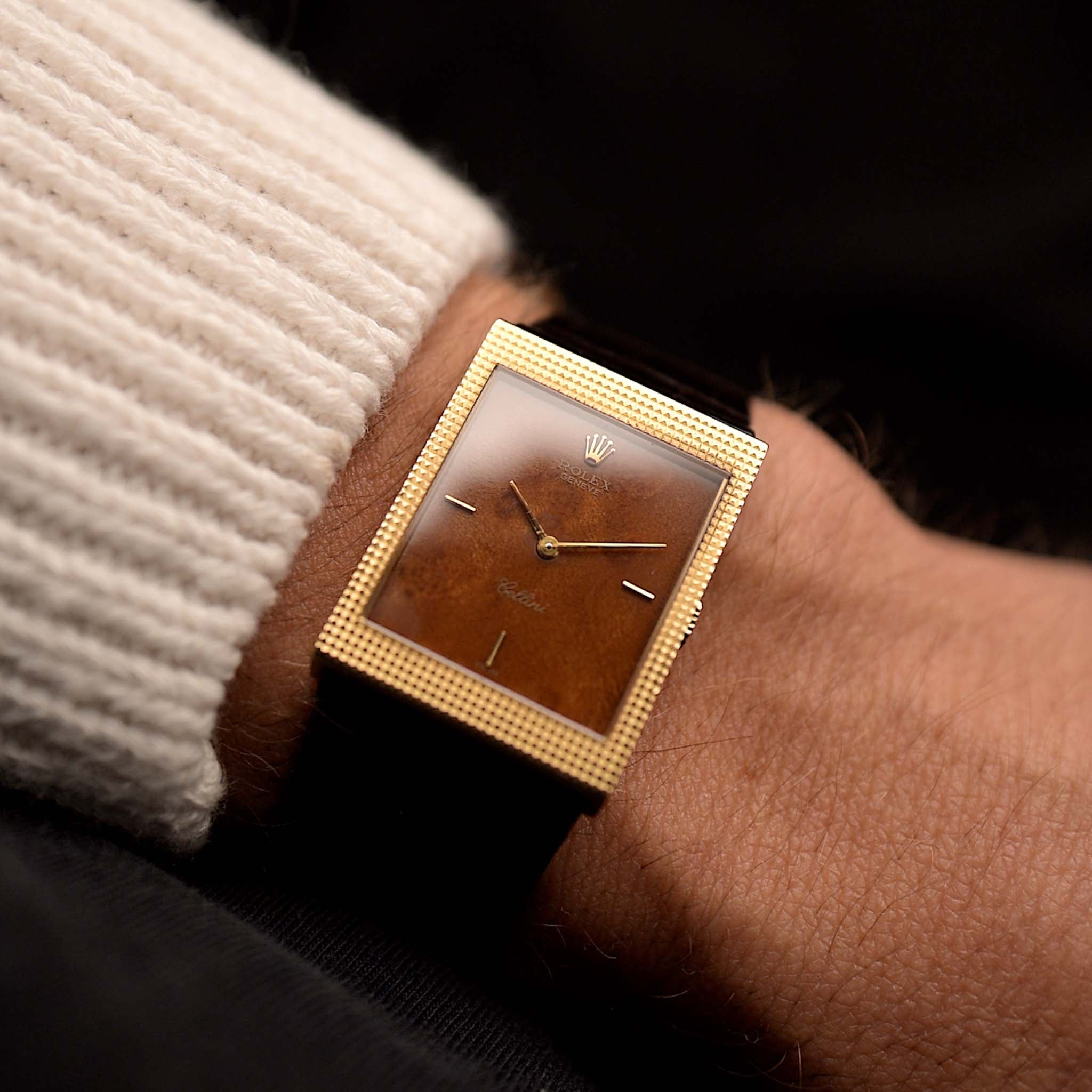 ساعة رولكس سيليني 4127 خشب عتيقة من رولكس سيليني من عام 1990 على معصم. علبة من الذهب الأصفر عيار 24 مم بعلبة من الذهب الأصفر عيار 18 قيراط، وميناء خشبي لا تشوبه شائبة، وحركة تعبئة يدوية وحزام جلدي من رولكس بني اللون.