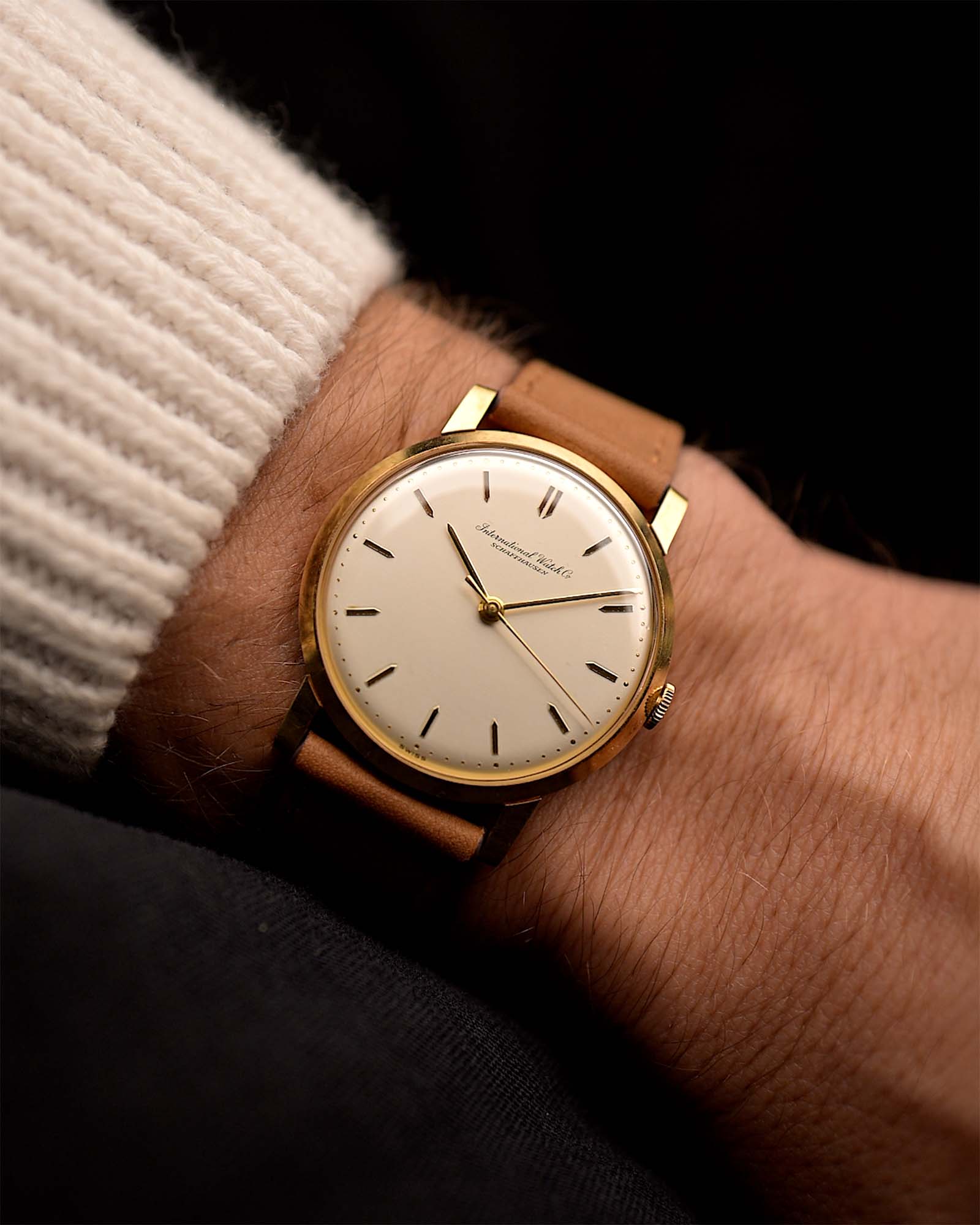 Vintage IWC Cal. 401 Dress Watch R1205 18k from 1964 on a wrist on black background. 33mm wide with 18k Yellow Gold Case, Manual Caliber 401 Movement, Flawless Silver Dial and Cognac Brown Leather Strap.
