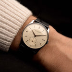 Close-up of a wrist wearing a Vintage IWC Cal. 83 Sub Second watch from 1940 with a black leather strap against a dark background. 32mm wide, Stainless Steel case with Manual Cal. 83 movement, Silver dial and Black Leather Strap.