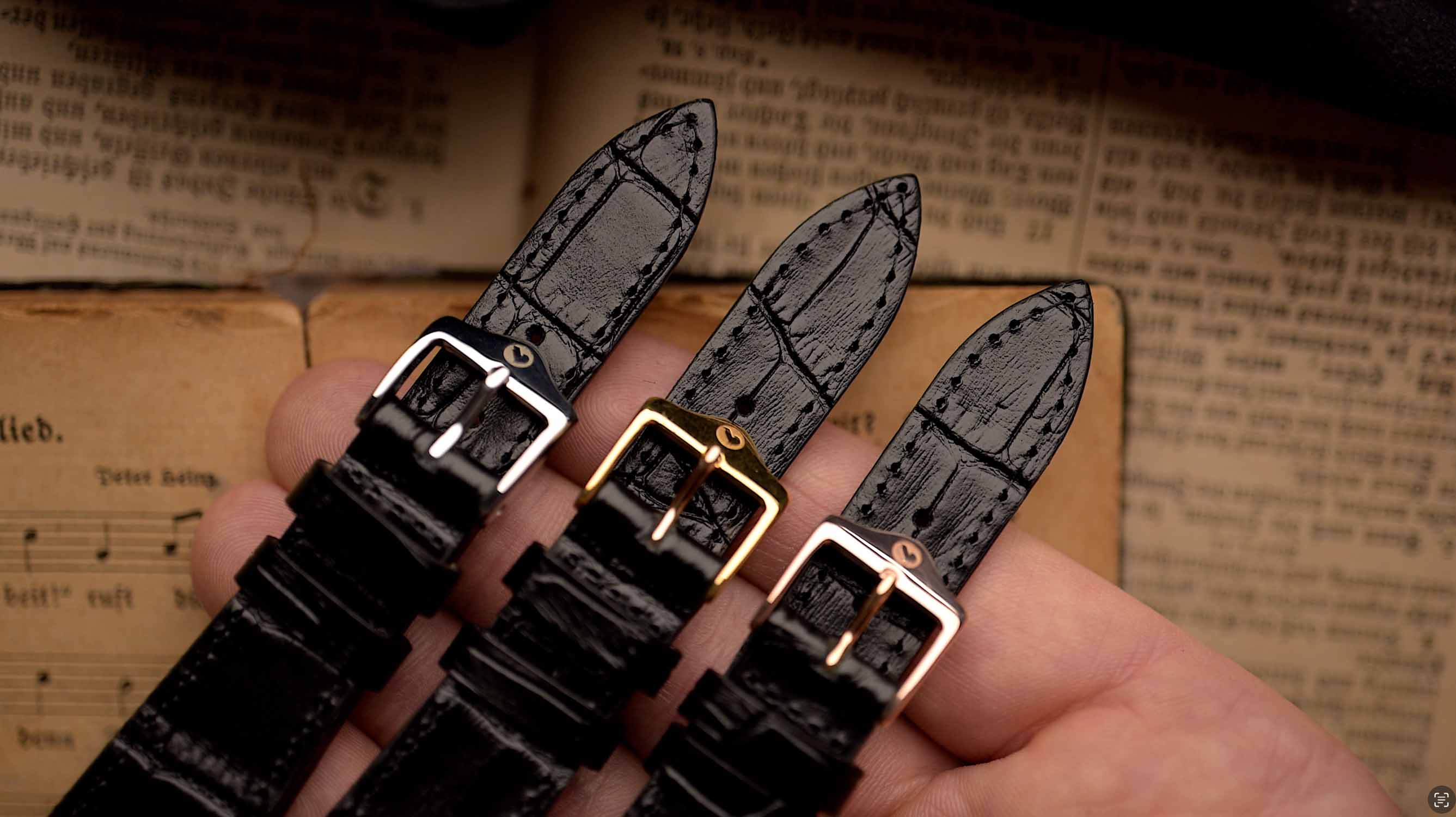 Tres correas de reloj negras con hebillas doradas sujetas sobre un libro abierto.