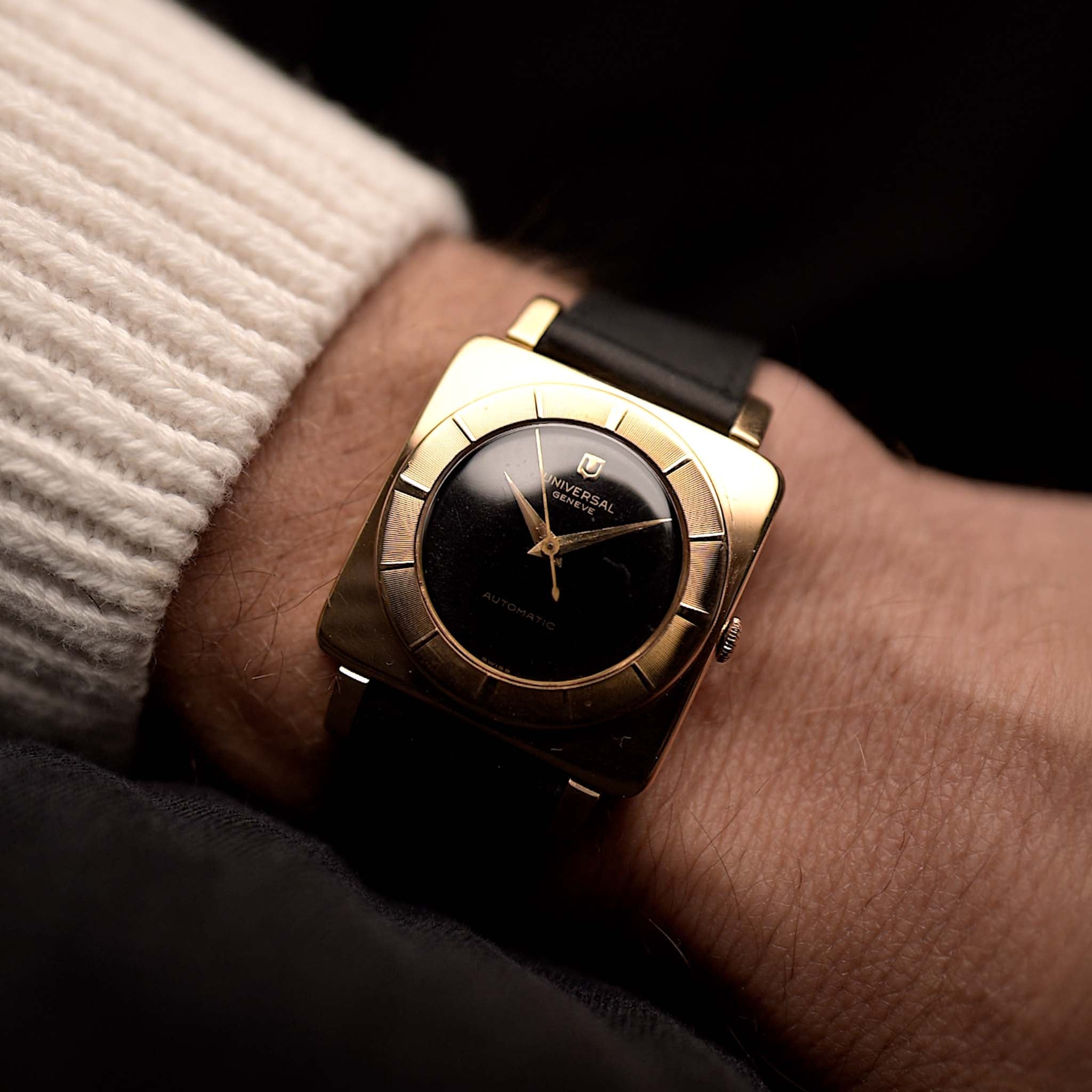 Genéve Universal 10237 Cioccolatone de 1956 de pulsera sobre fondo negro. 30 mm de ancho con caja de oro rosa de 18 quilates, movimiento de cuerda manual, esfera negra y correa de piel negra.