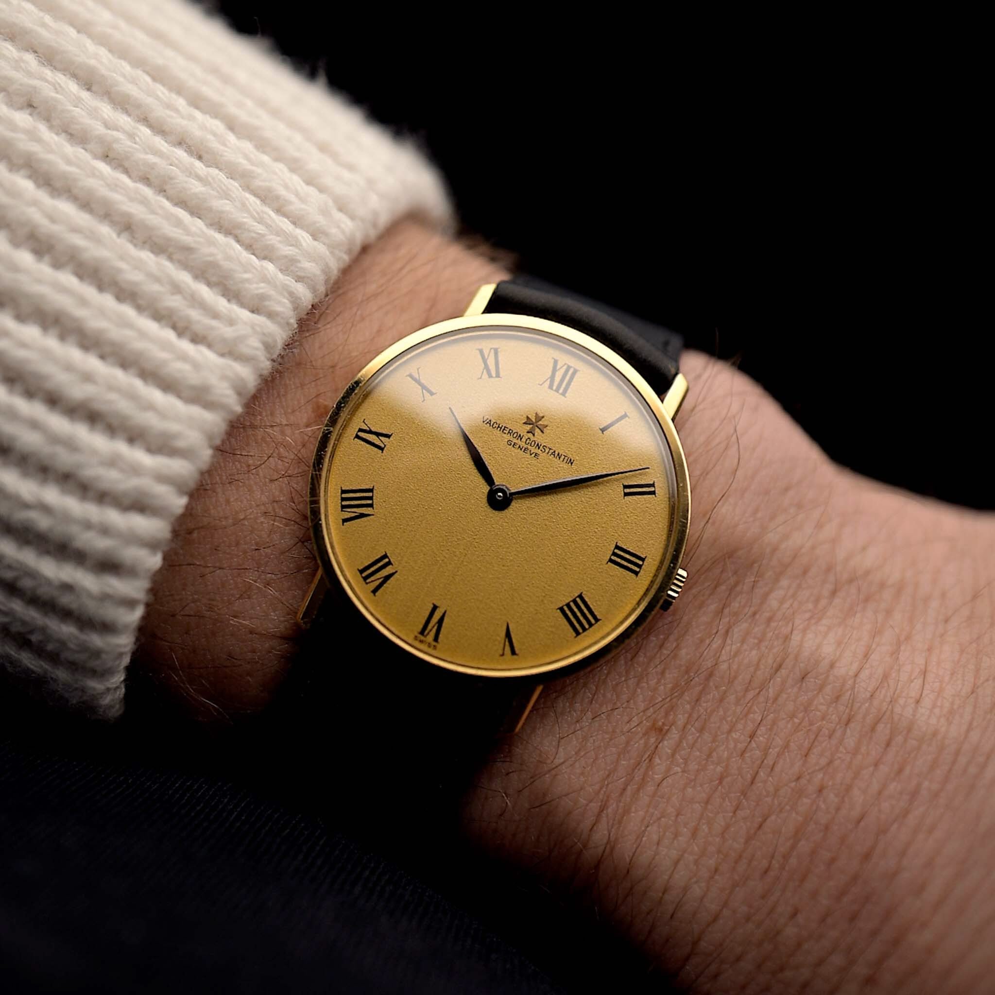 Vacheron Constantin 39009 Reloj Antiguo Roman de los años 80 de pulsera sobre fondo negro. 33mm de ancho con caja de oro amarillo de 18k, Esfera impecable cepillada dorada, Cal. 1015 Movimiento de cuerda manual y correa de piel negra.