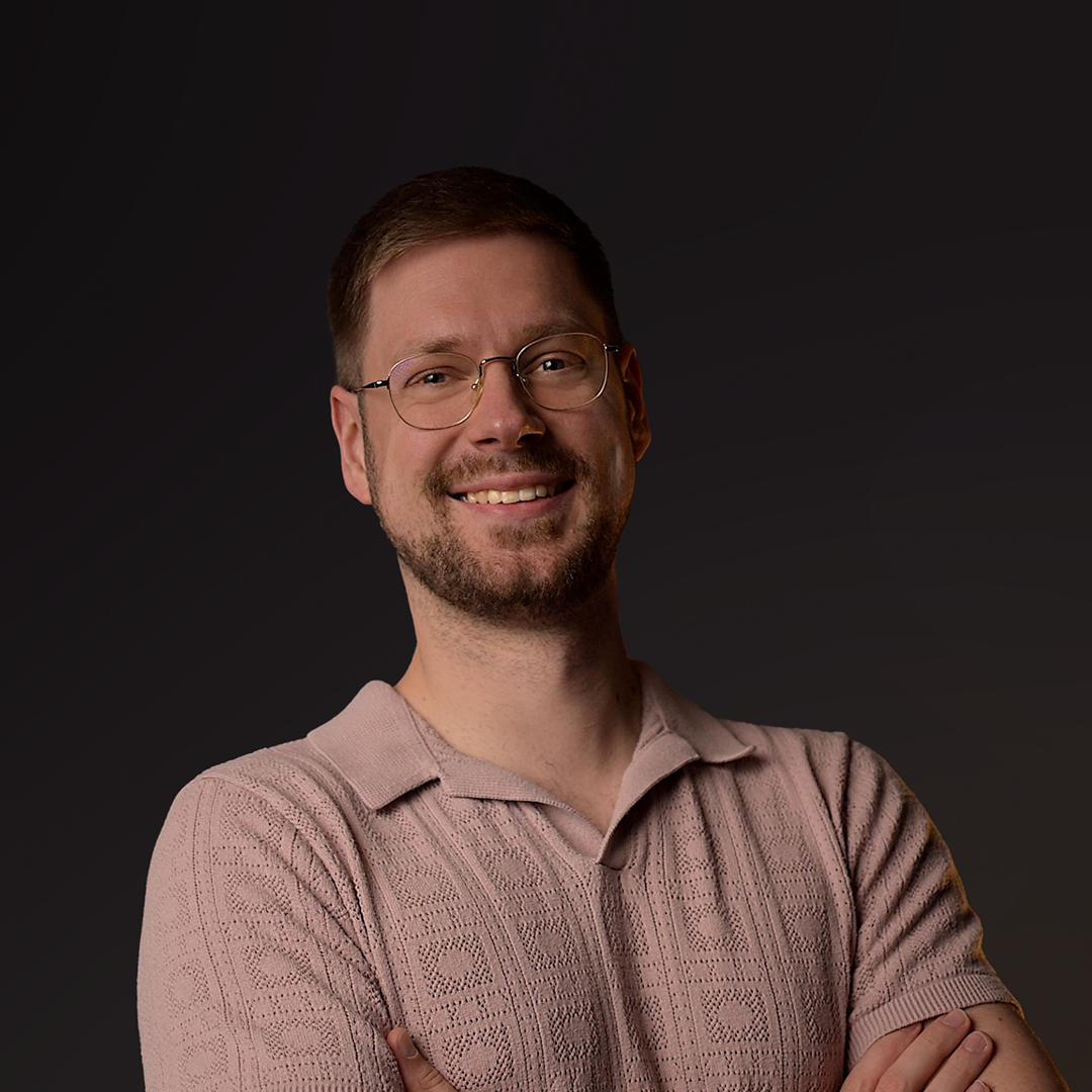 Hombre con gafas y jersey rosa sobre fondo oscuro