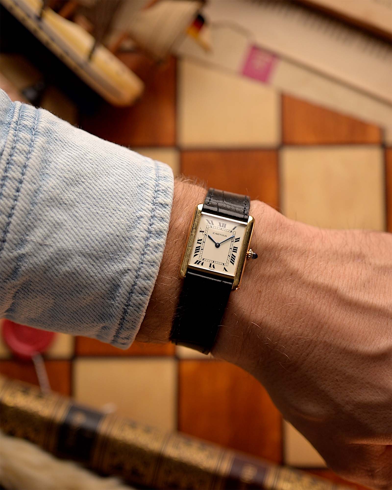 Persona che indossa un Cartier 78086 Tank Louis Paris vintage degli anni '70 con un pavimento a scacchi sullo sfondo