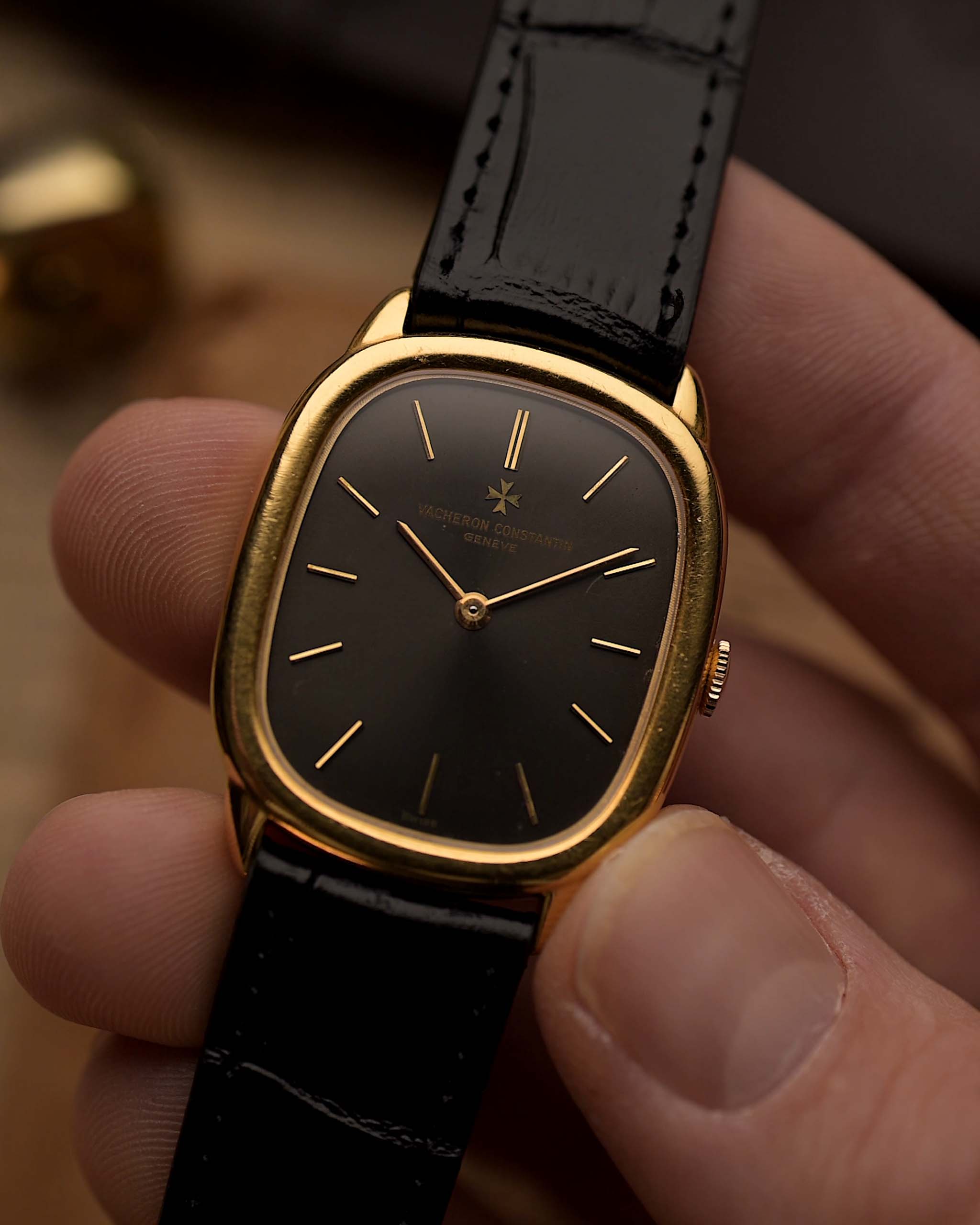 ساعة Vacheron Constantin 39007 Ellipse عتيقة من الذهب عيار 18 قيراط، بعلبة بيضاوية الشكل، وميناء رمادي، وحزام جلدي أسود، موضوعة على يد أمام خلفية ضبابية.