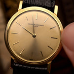 ساعة Vacheron Constantin Patrimony 6351 عتيقة ذات علبة مستديرة رفيعة من الذهب عيار 18 قيراطًا، تُحمل بيد على خلفية ضبابية