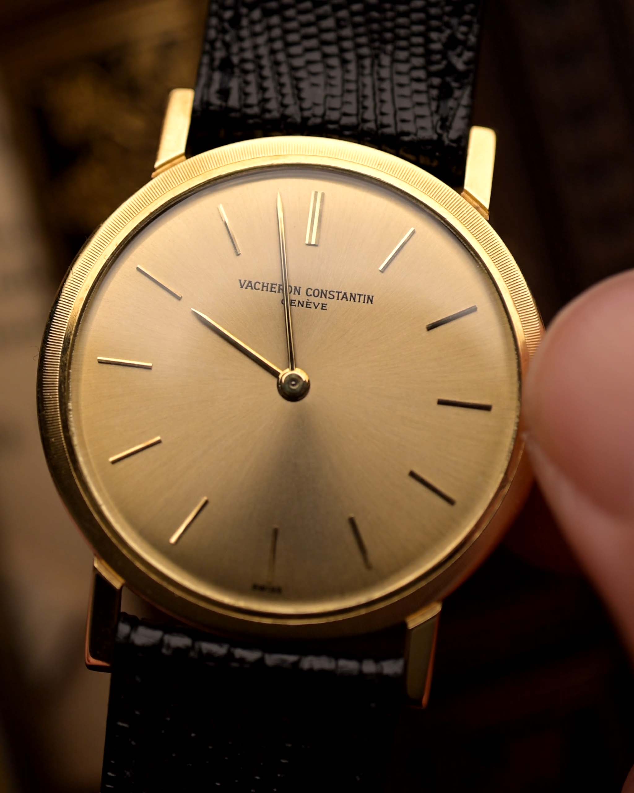 ساعة Vacheron Constantin Patrimony 6351 عتيقة ذات علبة مستديرة رفيعة من الذهب عيار 18 قيراطًا، تُحمل بيد على خلفية ضبابية