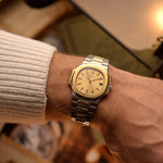 Vintage Patek Philippe Nautilus 3800 watch in two-tone gold and stainless steel, golden ribbed dial, automatic movement, on wrist, blurred background