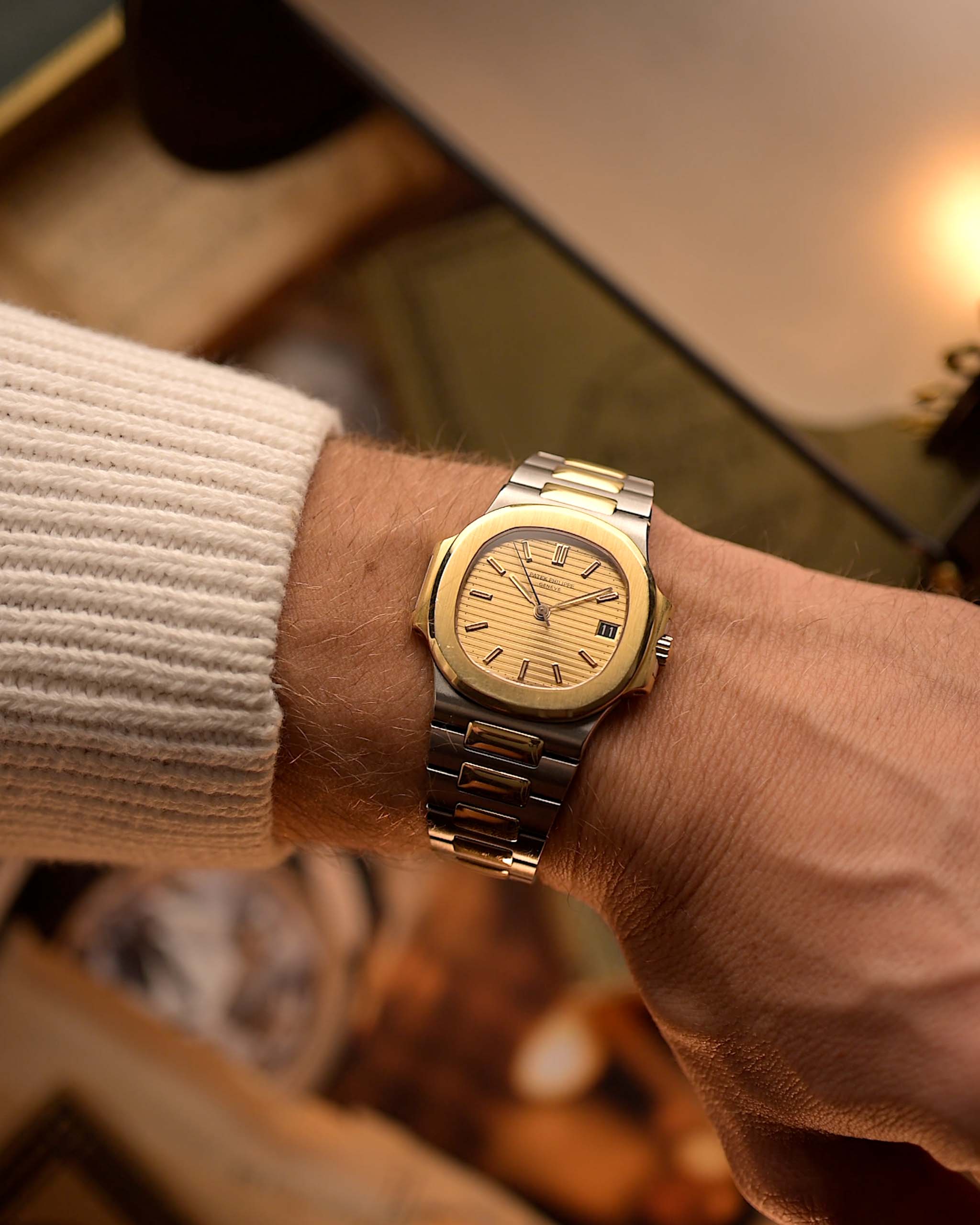 Vintage Patek Philippe Nautilus 3800 watch in two-tone gold and stainless steel, golden ribbed dial, automatic movement, on wrist, blurred background