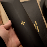Black box with a gold emblem held by a hand, with a blurred background