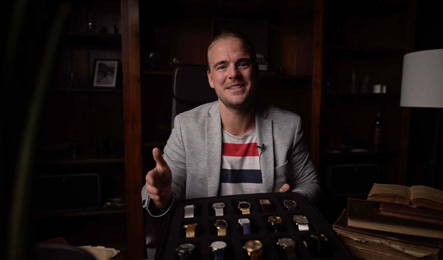 Man presenting wristwatches at a table, speaking to camera.