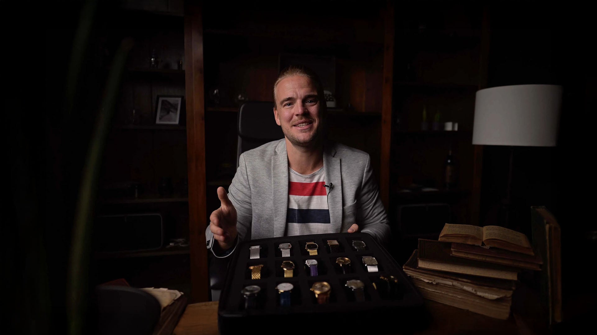 Man presenting wristwatches at a table, speaking to camera.