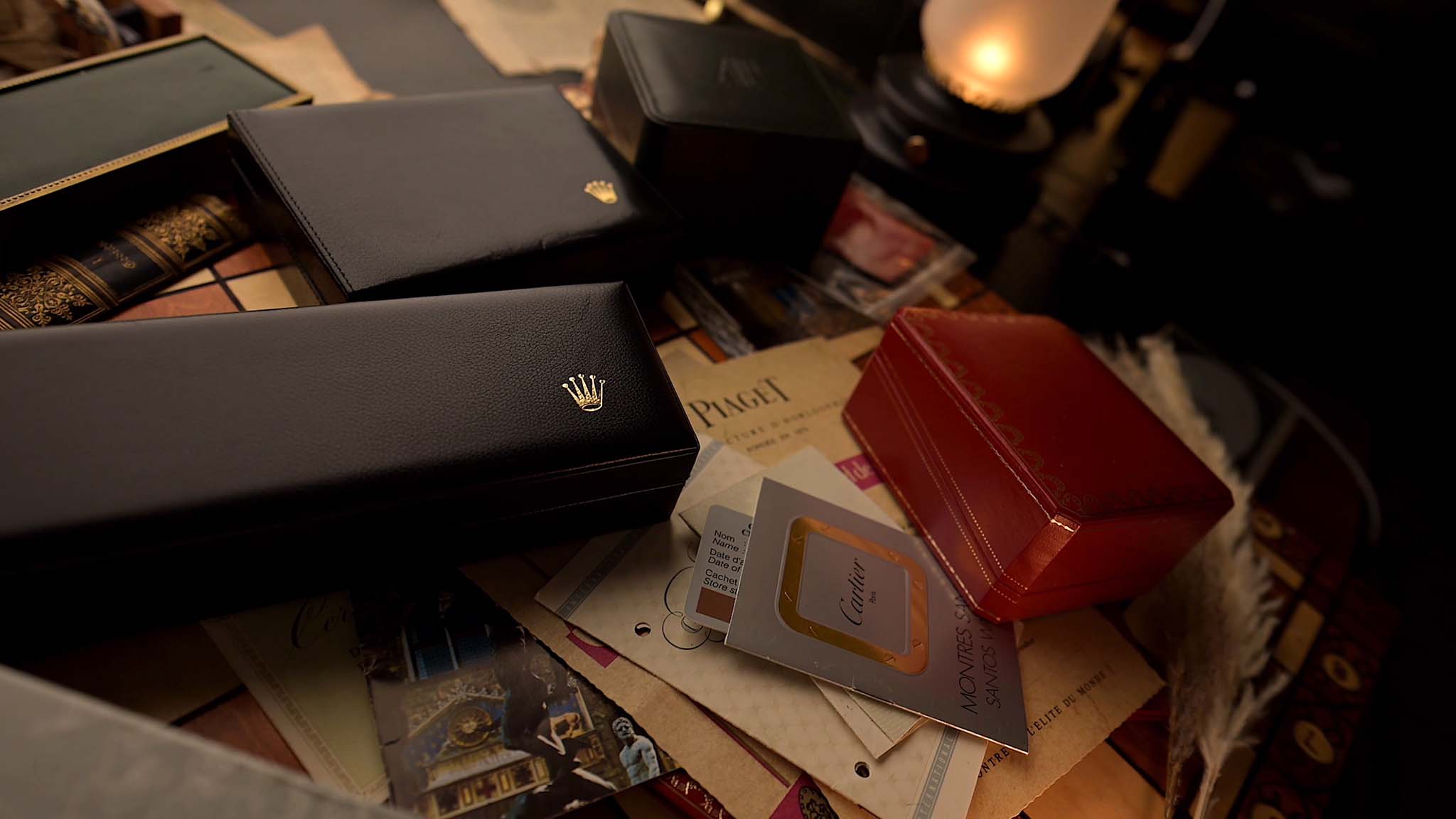 Luxury watch boxes, papers, and accessories arranged on a table in warm lighting.