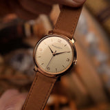Gros plan sur une Montre Vintage IWC Cal. 89, en or 18 carats , cadran blanc/argenté, tenue par une main sur un fond flou