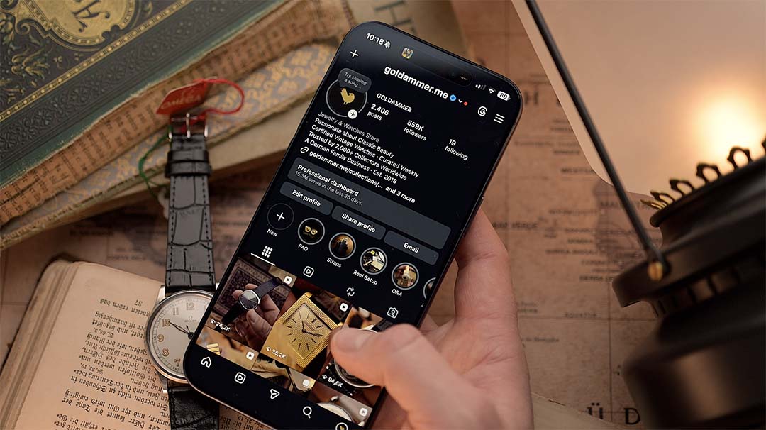 Person holding a smartphone with a instagram app interface on a desk with books and a lamp.