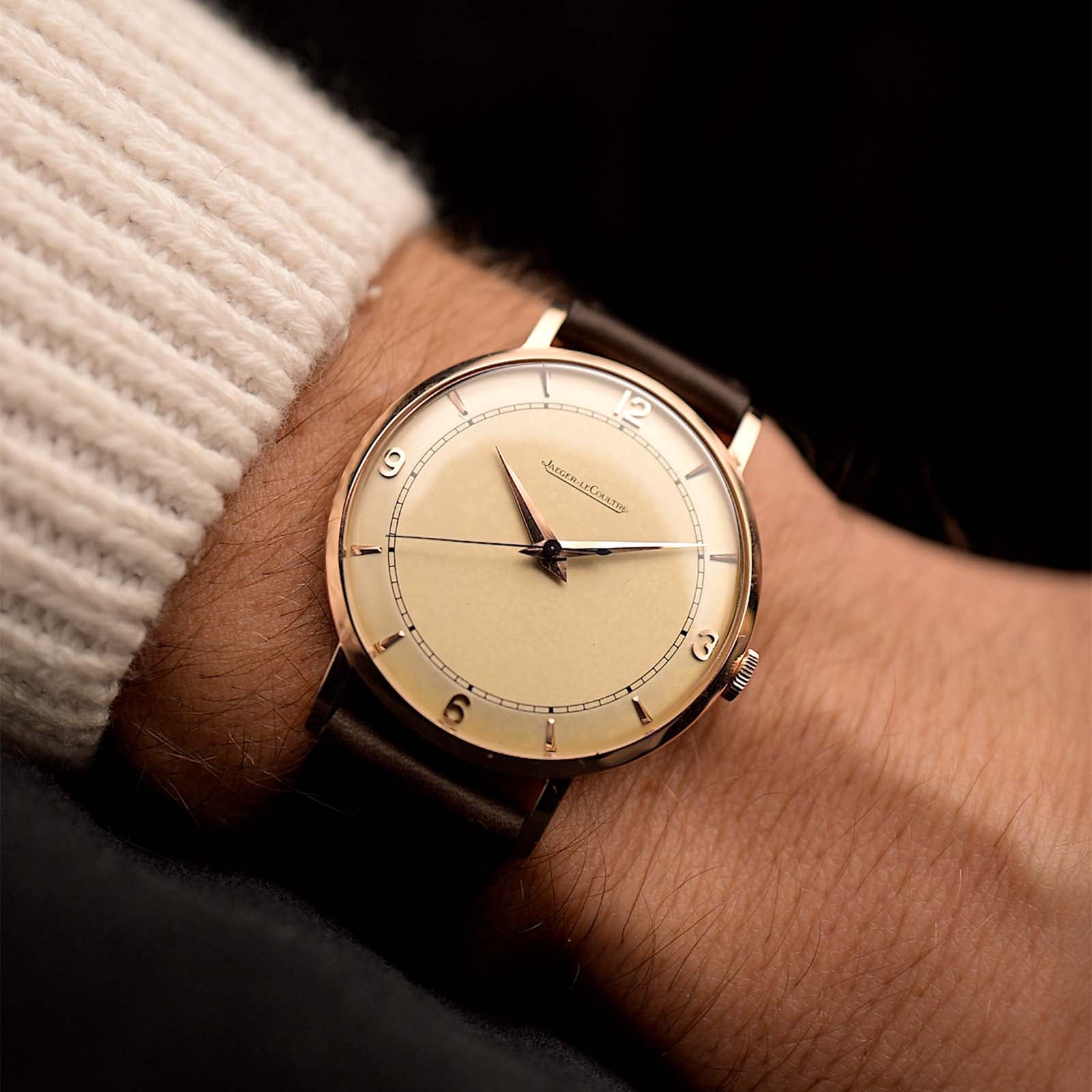 Rosegold Vintage Jaeger LeCoultre 18k Rose Railroad watch from the 1950s on a person's wrist with a dark background. 35mm wide with 18k Rose Gold Case, Manual Wind Caliber P450/4C, Cream Dial and Brown Leather Strap.