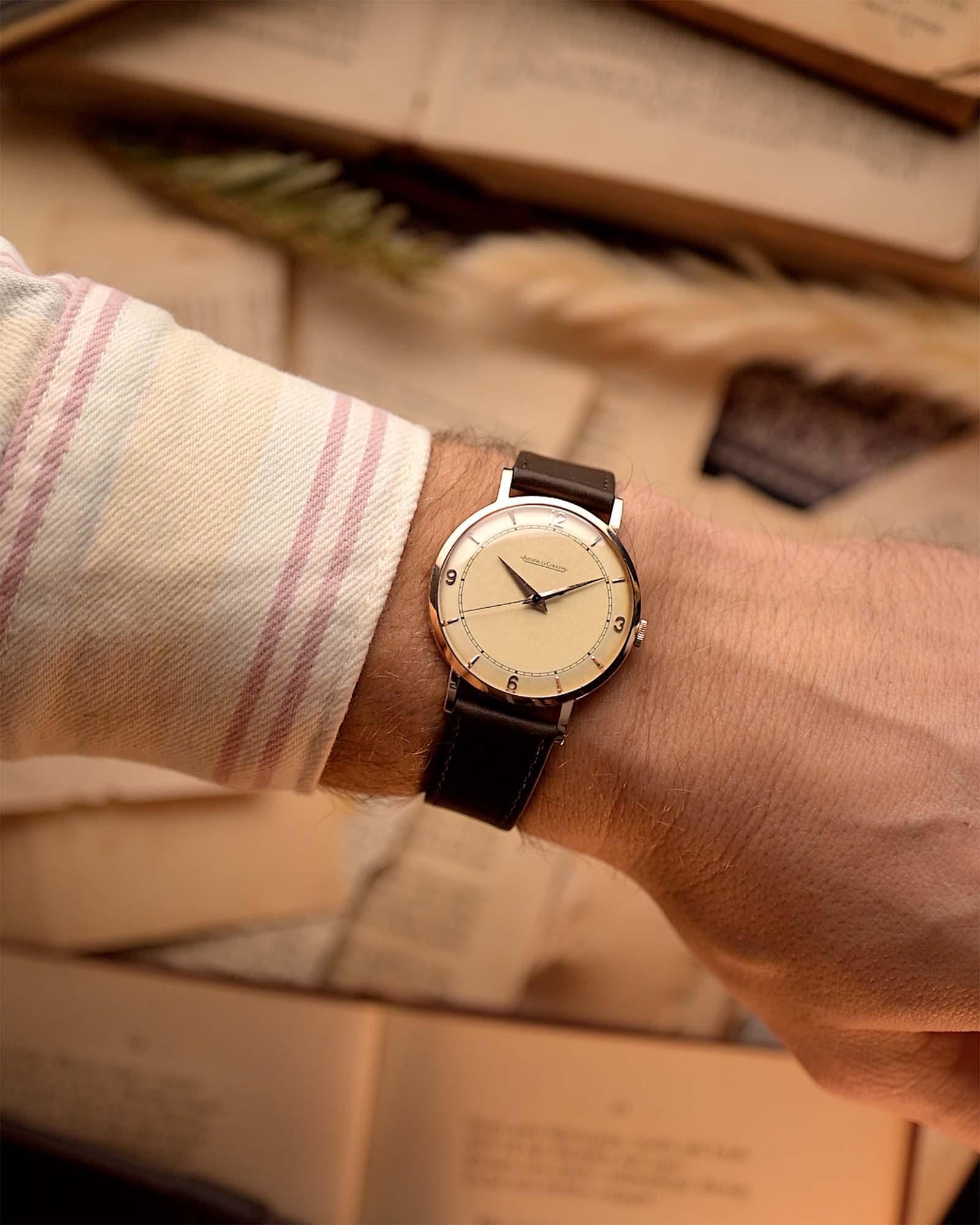 Rosegold Vintage Jaeger LeCoultre 18k Rose Railroad watch from the 1950s on a person's wrist with a beige background.