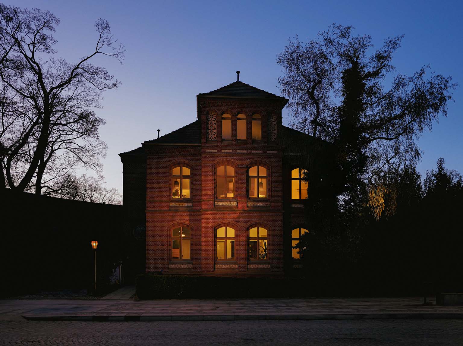 Dunkles Gebäude mit beleuchteten Fenstern bei Nacht, umgeben von Bäumen