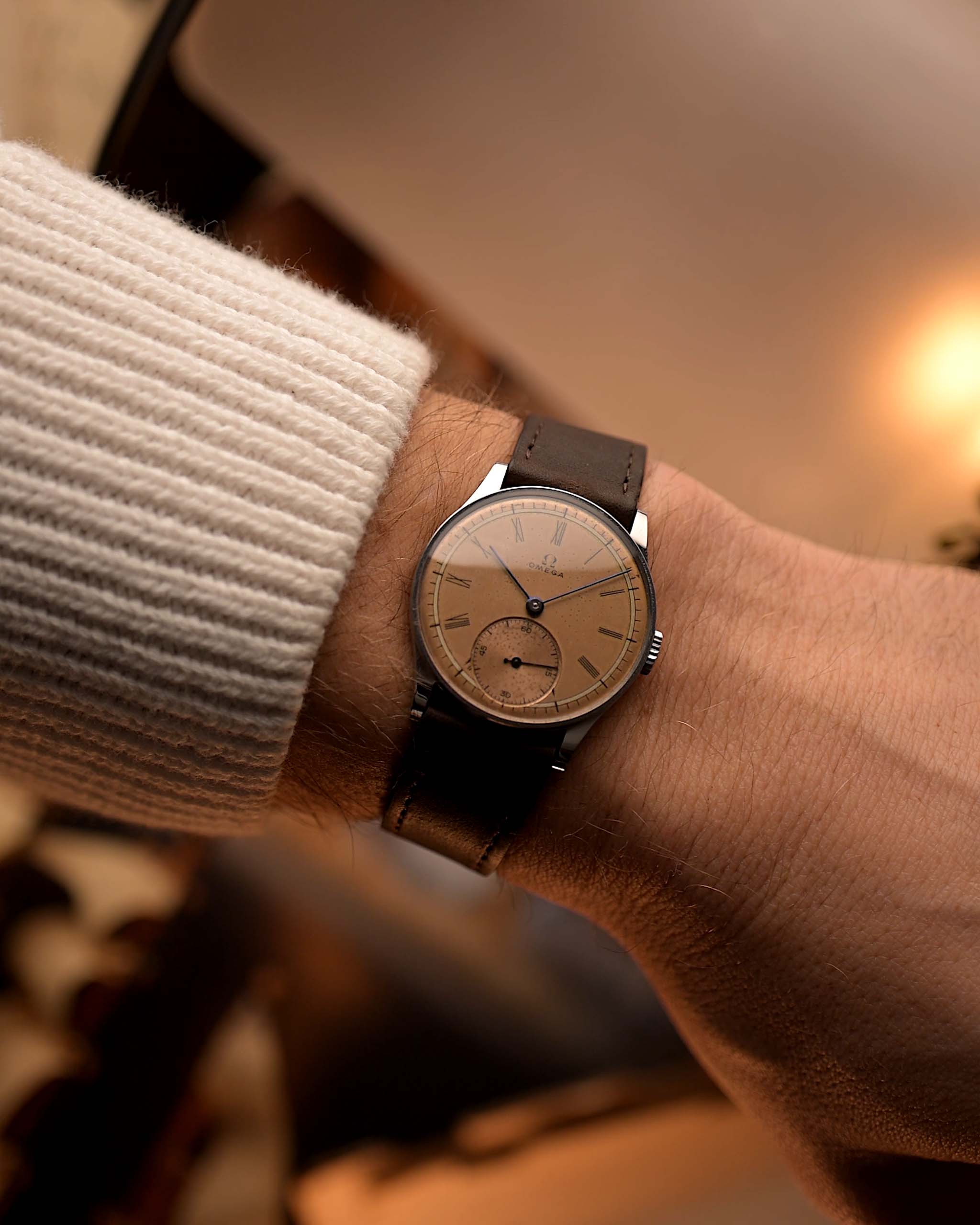 Vintage Omega Art Deco watch featuring a salmon dial, stainless steel case, manual wind movement, and brown leather strap on wrist on blurred background