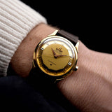 Photo of a Omega Constellation 2852 Pie Pan Arrow from 1956 on a wrist. 35mm case in Yellow Gold Case, Automatic Chronometer Caliber 505, Gold Pie Pan Dial, Brown Leather Strap.