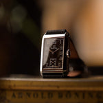 Vintage Omega Rectangular Syringe watch, black gilt dial, stainless steel case, on a wooden surface with a blurred background