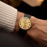 Piaget Altiplano 9036, 18k gold with golden sunburst dial, worn on the wrist over a warm backdrop