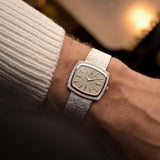 Montre Piaget 9574 TV, en or 18 carats avec cadran martelé, portée au poignet sur un fond aux teintes chaudes