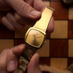 Vintage Rolex Cellini 4084 watch, square  case in 18k yellow gold case, golden dial, manual, gold bracelet held in against a wooden background