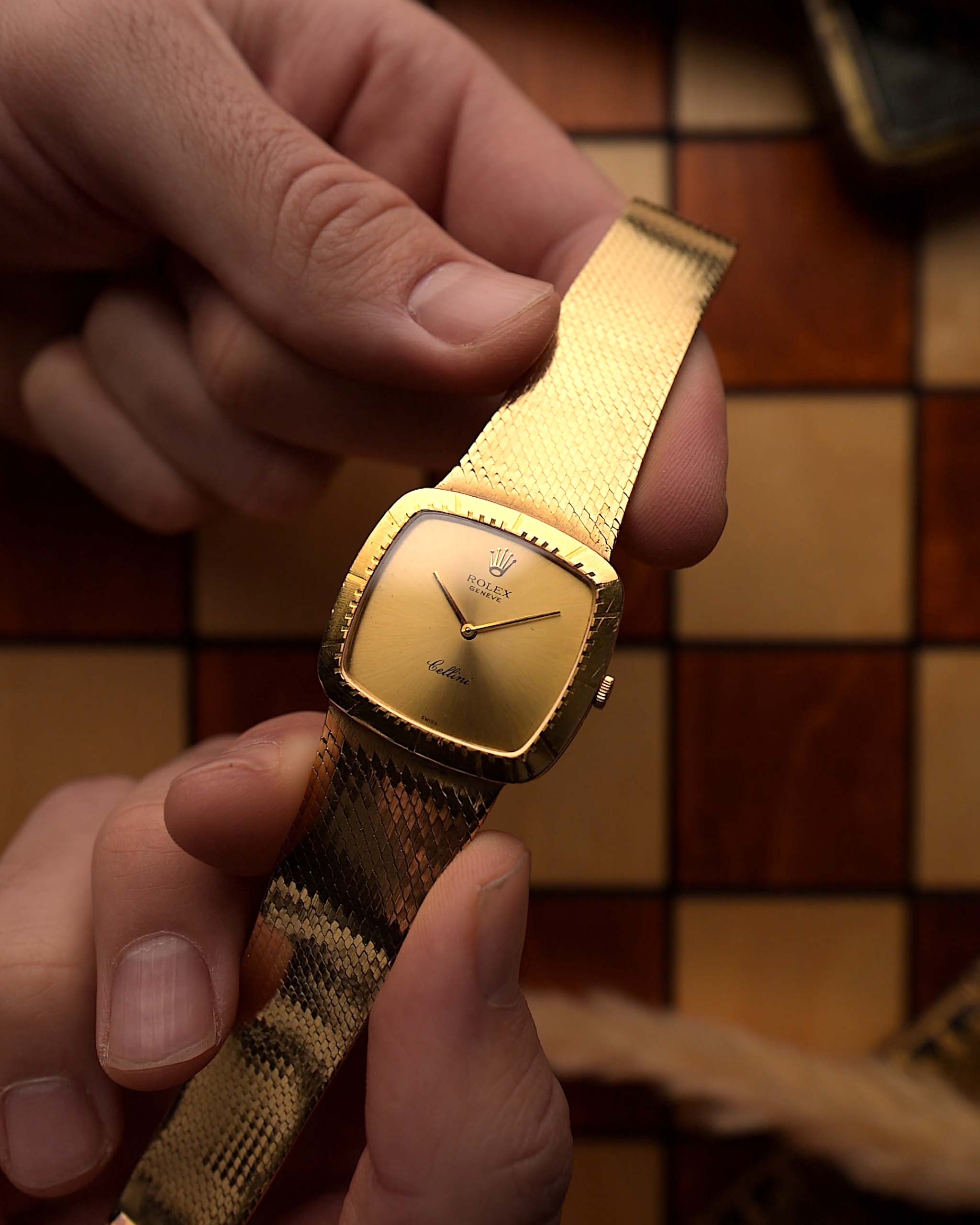 Vintage Rolex Cellini 4084 watch, square  case in 18k yellow gold case, golden dial, manual, gold bracelet held in against a wooden background