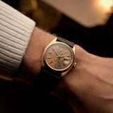 Rolex Day-Date 18038, 18k yellow gold with Havana dial, worn on the wrist over a warm backdrop