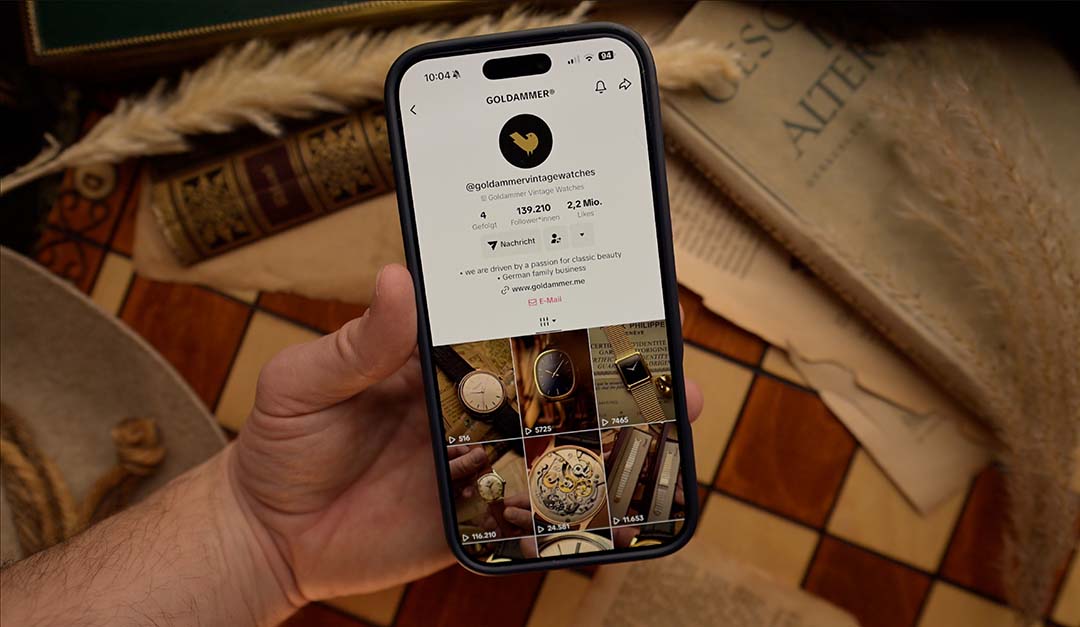 Hand holding a smartphone displaying a Goldammer tiktok profile on a textured surface.