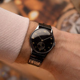 1941年款 Universal Genève 21246 復古腕錶，不鏽鋼錶殼，黑色鍍金錶盤，手動上鏈機芯，錶帶佩戴於手腕上，背景為模糊效果