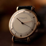 Close-up of Vintage Vacheron Constantin Teardrop watch in 18k rose gold, white-silver dial, manual Cal. V454, on black strap, blurred background