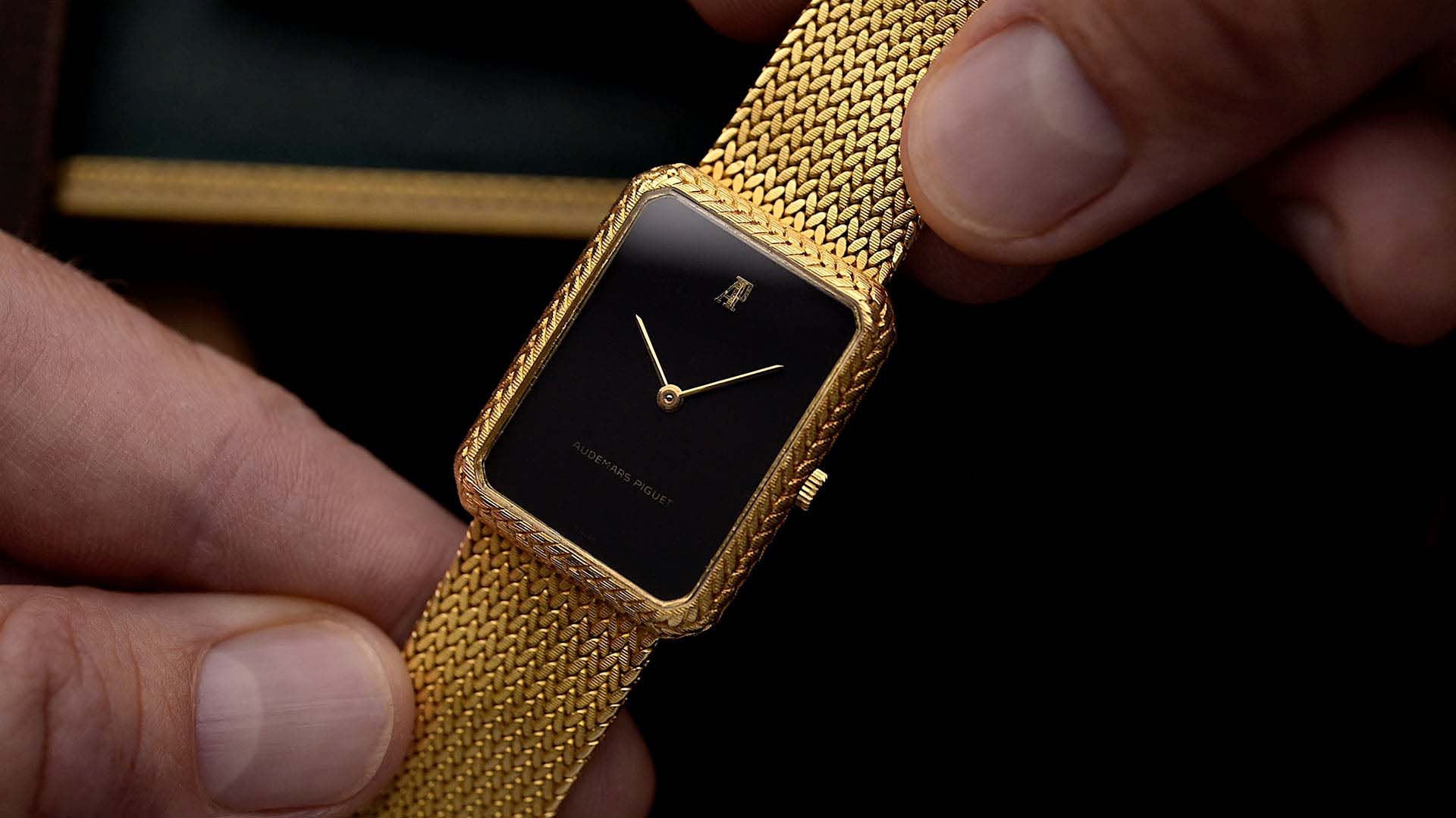 Gold rectangular wristwatch with black dial.