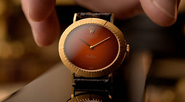 Orologio da polso in oro con quadrante marrone, tenuto in mano su uno sfondo sfocato