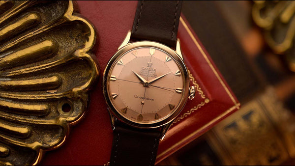 Vintage watch with a gold case and black leather strap on a textured surface.