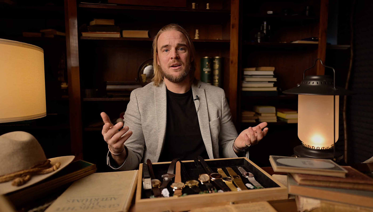Man sitting at a desk with a box of items, surrounded by books and a lamp in a dimly lit room.