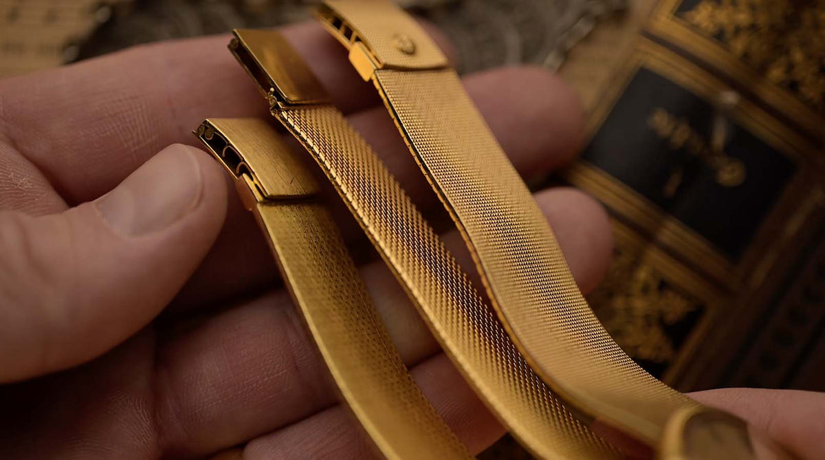 A close-up of three gold watch bracelets held in a hand.