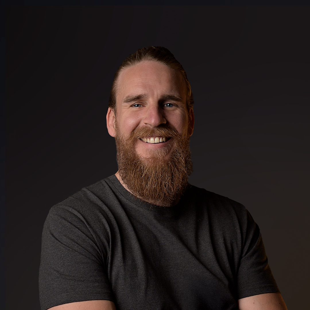 Man with a beard wearing a dark gray t-shirt against a black background