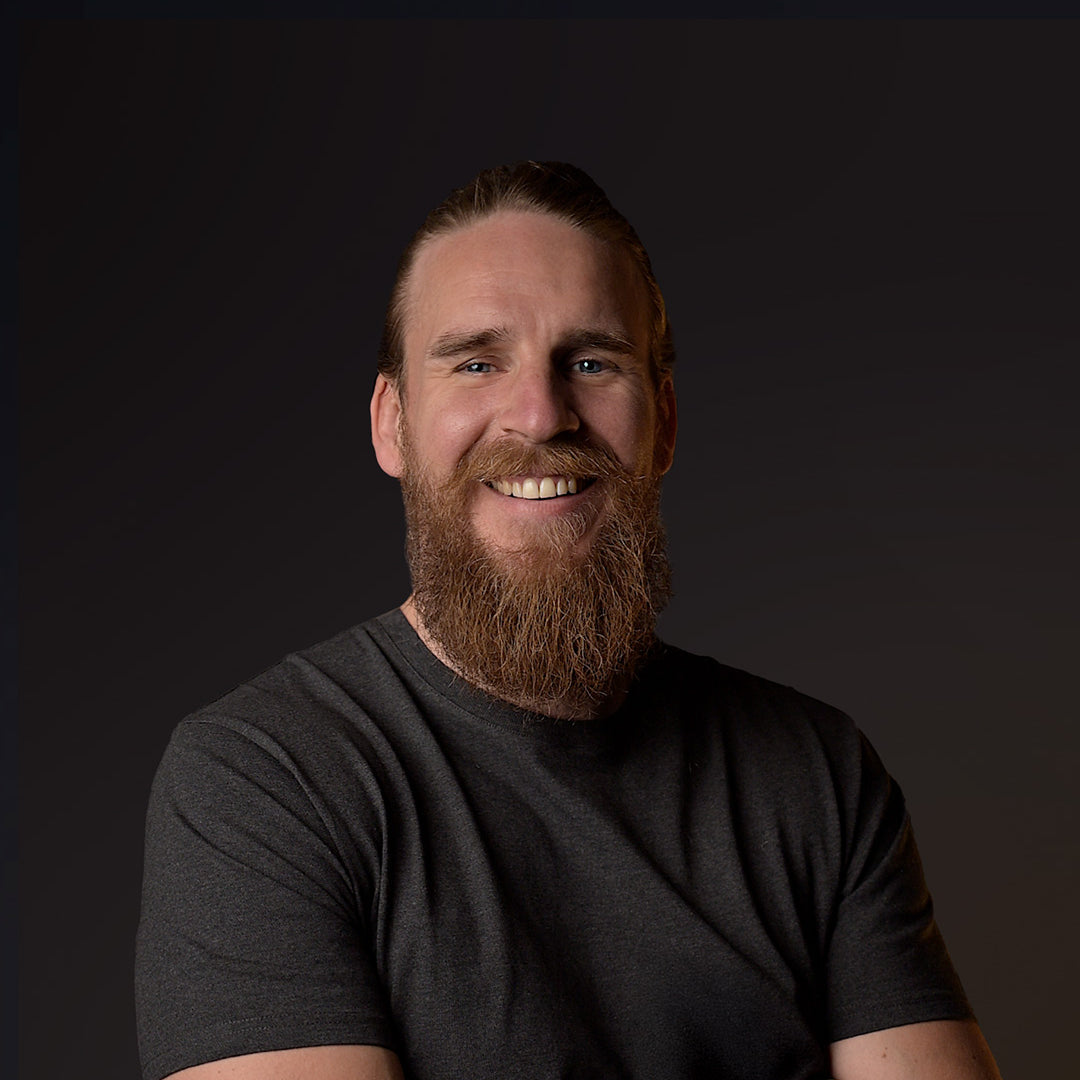 Man with a beard wearing a dark gray t-shirt against a black background