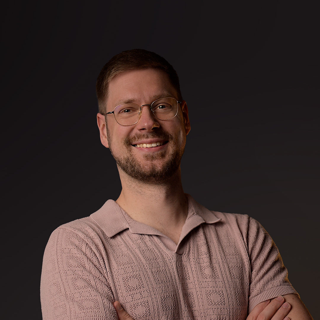 Man wearing glasses and a pink polo against a dark background