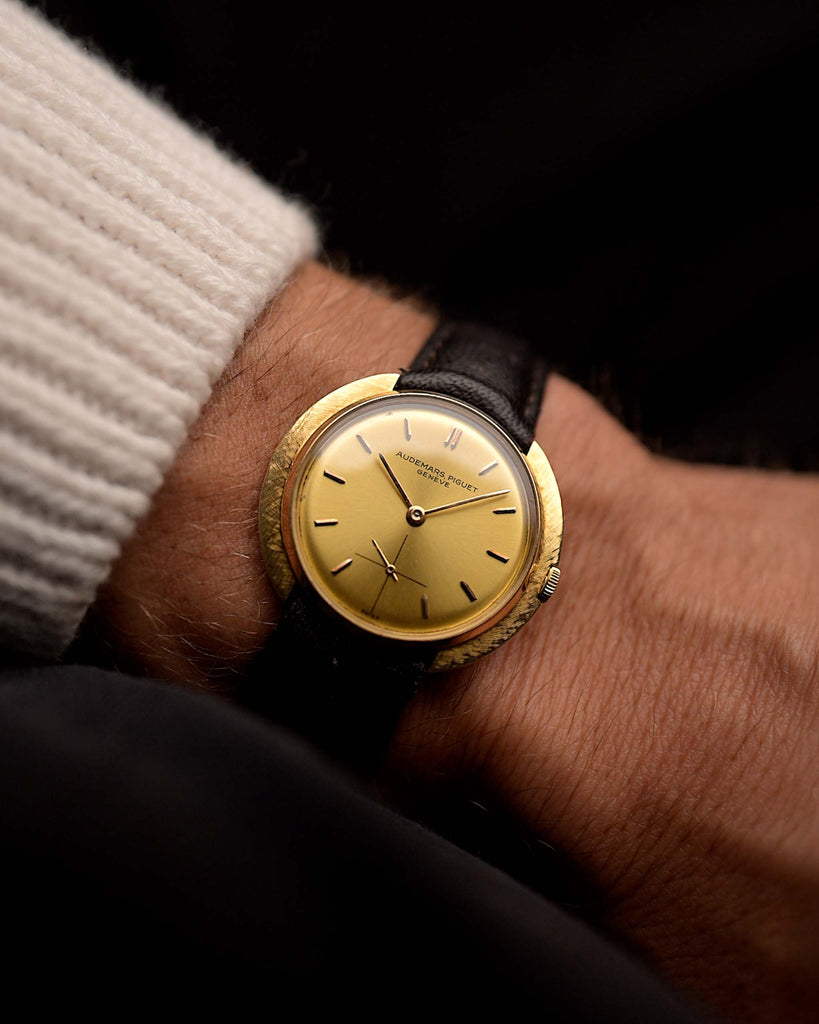 Vintage Audemars Piguet Disco Volante watch 18k gold from the 1960s on a wrist. 32mm wide, 18k Yellow Gold Case, Manual Wind Caliber K2001, Golden Sunburst Dial and Black Leather Strap.