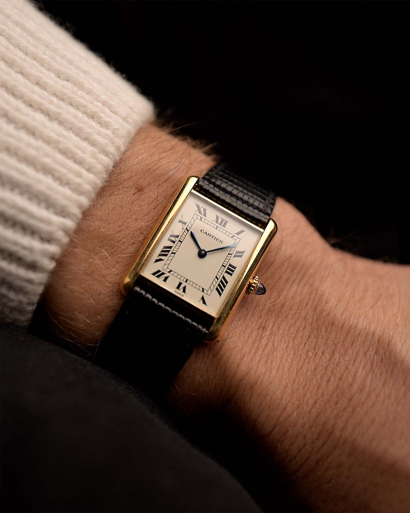 Vintage Cartier 78086 Tank watch Louis Paris from the 1970s on a wrist on black background. 23.5 x 29.5 mm with 18k Yellow Gold Case, Manual Wind Movement, Flawless White Cartier Paris Dial and black Leather Strap.
