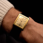 Gold Vintage Piaget 9653 Tank watch on a person's wrist with a dark background.