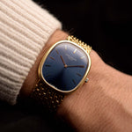 Patek Philippe 3738 Ellipse Jumbo Vintage Watch from the 1980s on a wrist on black background. 31mm wide with 18k Yellow Gold Case, Automatic Caliber 240, Flawless Blue Sunburst Sigma Dial and Yellow Gold Bracelet.