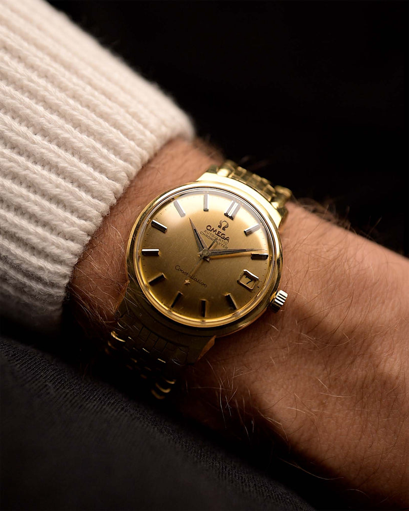 Vintage Gold Omega Constellation 14398 de Luxe watch Onyx from 1960 on a wrist on black background. 34mm wide, 18k Yellow Gold, Automatic Caliber 561 movement, Golden dial and Gold bracelet.