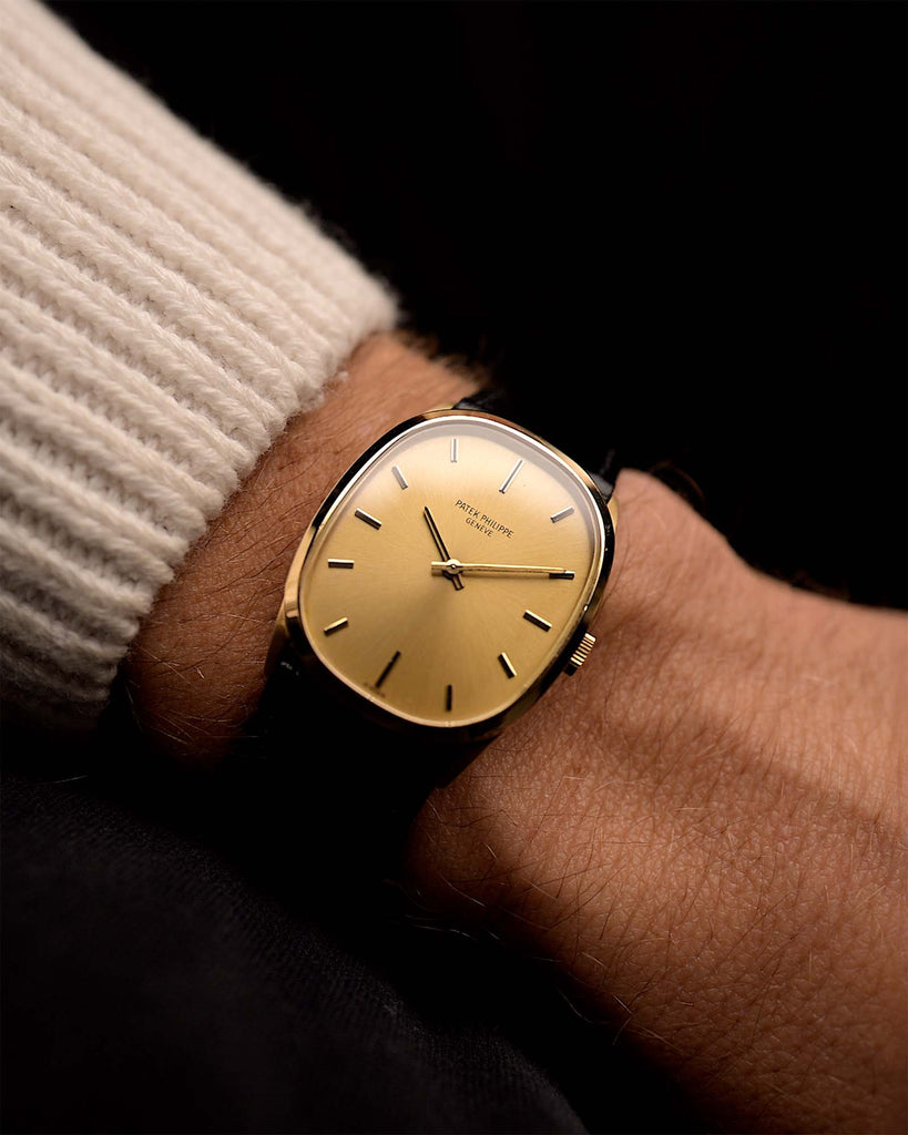 Gold Vintage Patek Philippe Ellipse 3546 Watch on a wrist from the 1970s. 27mm with 18k yellow gold case, Manual-wind Caliber 23-300, Flawless golden sunburst dial and Black Leather strap.