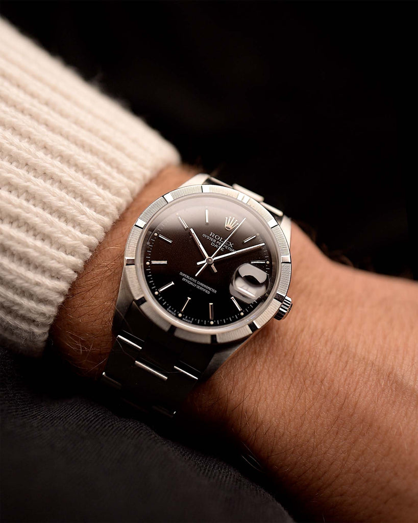 Stainless Steel Vintage Rolex Oyster Perpetual 15210 Date Black watch from 2002 on a wrist on black background. 34mm wide with Automatic Caliber 3135, Flawless black dial and Rolex Oyster bracelet.