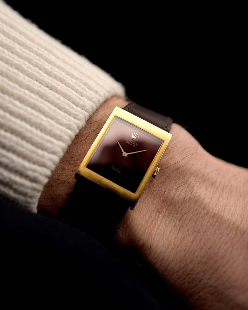 Rolex Cellini 4014 vintage Watch from 1972 on a wrist on black background. 18k Yellow Gold Case, 22.5mm wide with Glossy Burgundy Dial, Manual Wind Movement and Dark Brown Leather Strap.